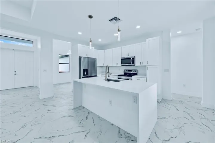 Kitchen featuring pendant lighting, sink, an island with sink, white cabinetry, and stainless steel appliances