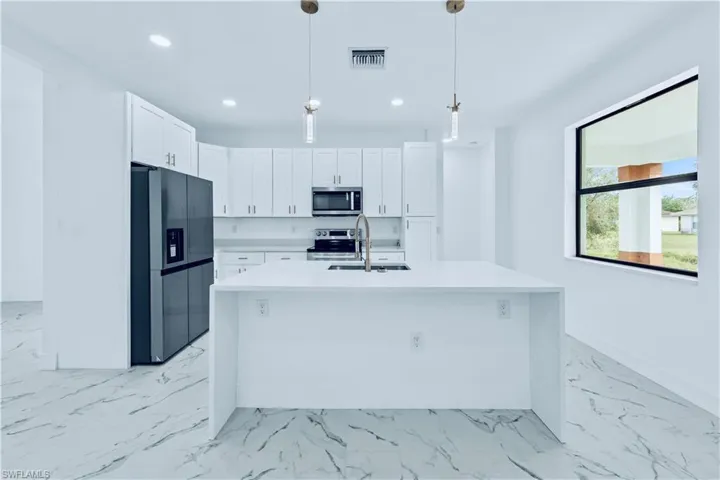 Kitchen featuring a kitchen island with sink, hanging light fixtures, sink, appliances with stainless steel finishes, and white cabinetry