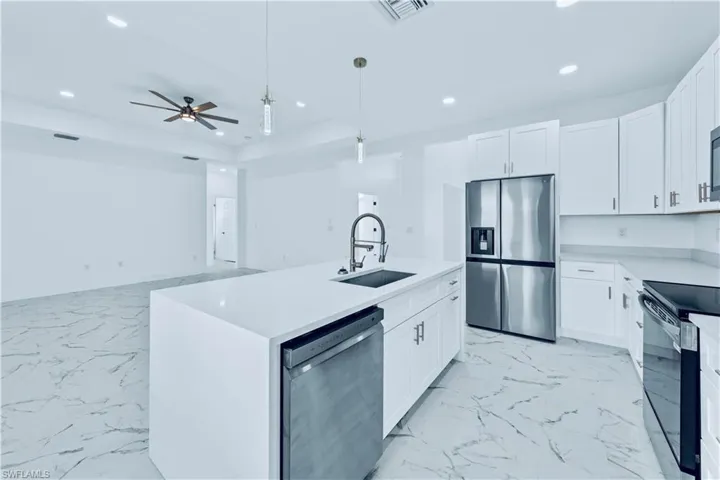 Kitchen with white cabinetry, sink, stainless steel appliances, decorative light fixtures, and a center island with sink