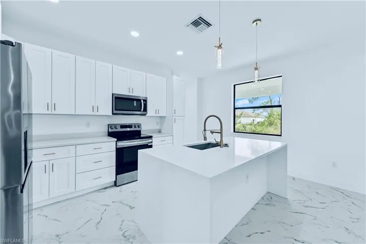 Kitchen with white cabinets, sink, stainless steel appliances, and a center island with sink