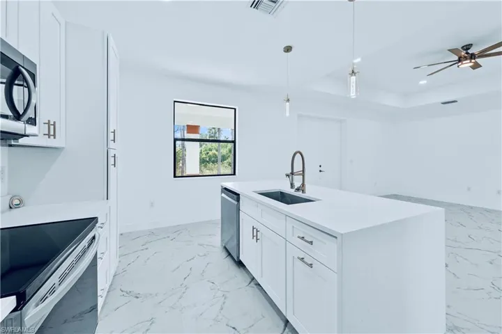 Kitchen with white cabinetry, sink, pendant lighting, a kitchen island with sink, and appliances with stainless steel finishes
