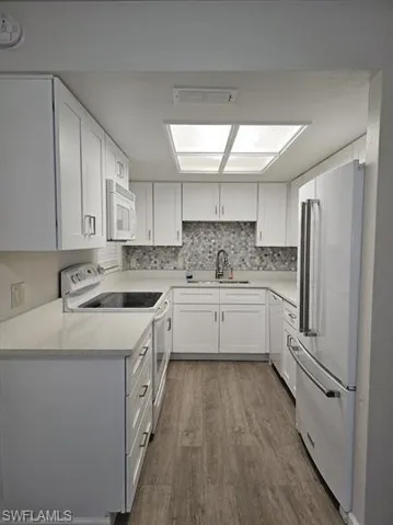 Kitchen with white cabinets, white appliances, dark wood finished floors, and light stone countertops