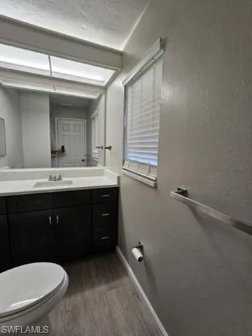 Half bathroom with vanity, dark wood finished floors, a textured ceiling, and a textured wall