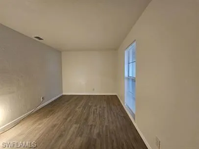 Spare room featuring dark wood-style floors and baseboards
