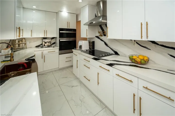 Kitchen with white cabinetry, modern cabinets, double oven, light marble finish floors, and light stone counters