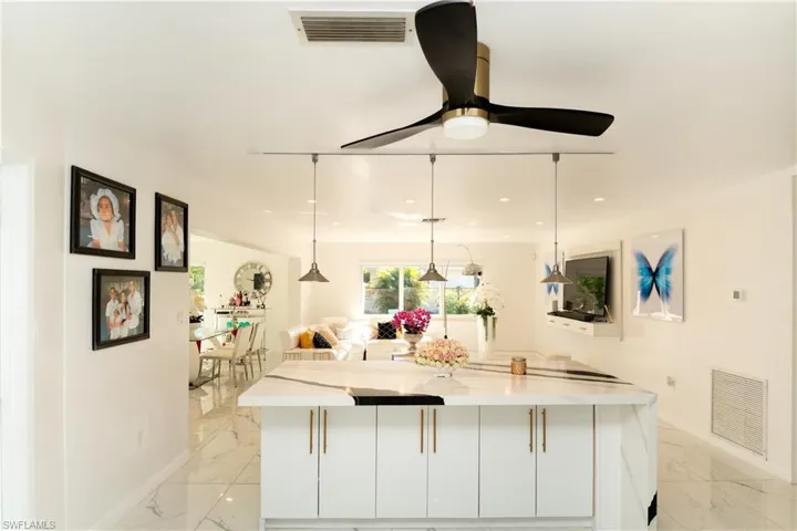Kitchen featuring pendant lighting, a kitchen island, white cabinetry, and light stone countertops