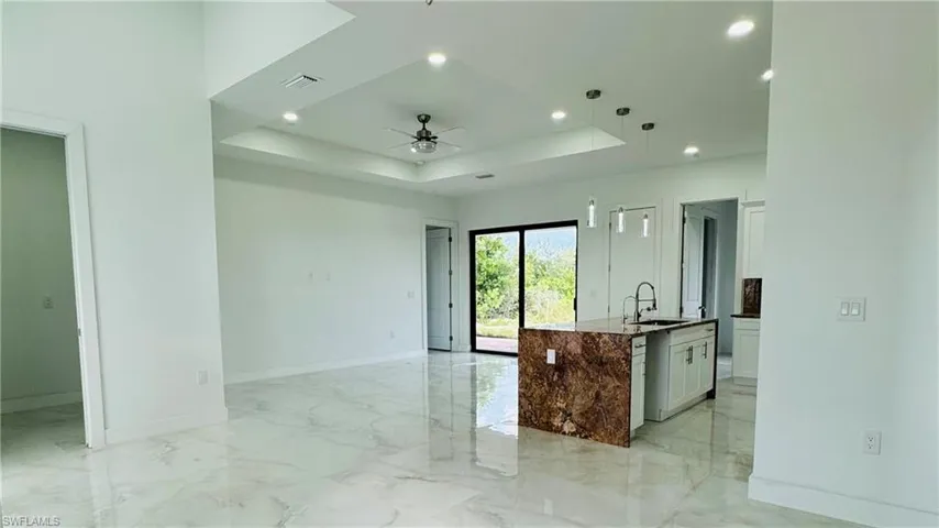 Kitchen featuring white cabinetry, hanging light fixtures, sink, an island with sink, and a tray ceiling