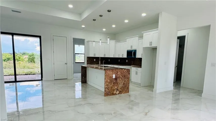Kitchen with white cabinetry, dark stone counters, backsplash, an island with sink, and hanging light fixtures