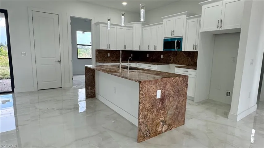 Kitchen featuring an island with sink, white cabinets, sink, and decorative backsplash