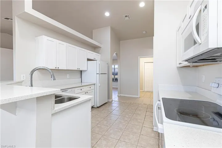 Kitchen featuring white appliances, arched walkways, white cabinets, light stone countertops, and a peninsula