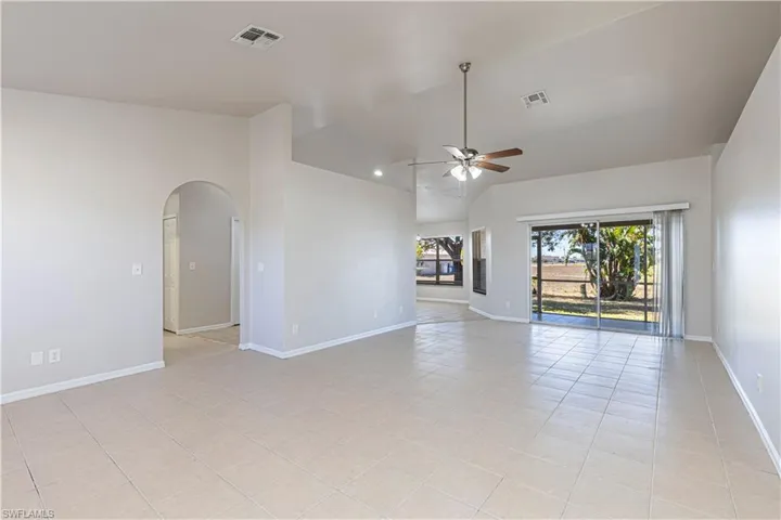 Empty room with arched walkways, a ceiling fan, light tile patterned flooring, and vaulted ceiling