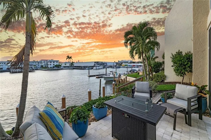Patio terrace at dusk with a water view, a dock, an outdoor fire pit, and a patio