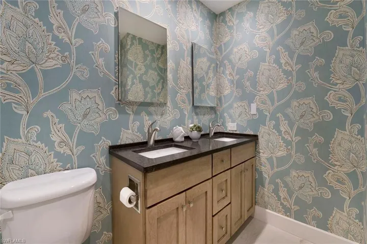 Bathroom with double vanity, wallpapered walls, and tile patterned flooring