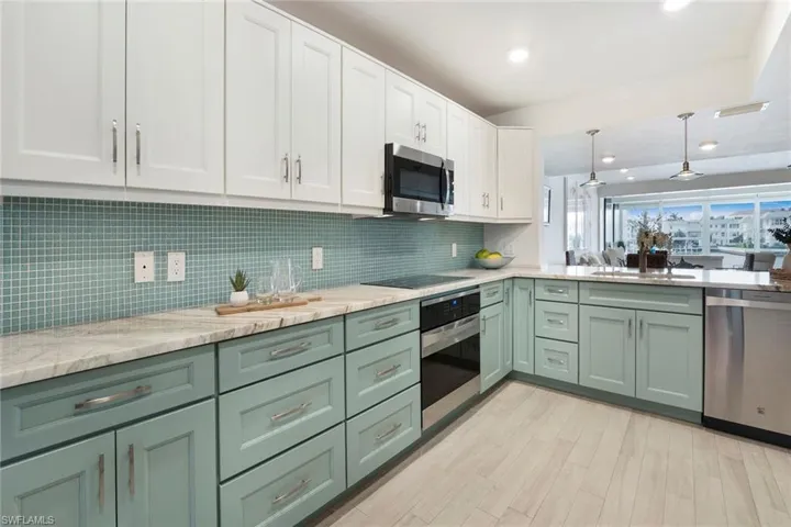 Kitchen with green cabinets, white cabinetry, stainless steel appliances, pendant lighting, and light stone countertops