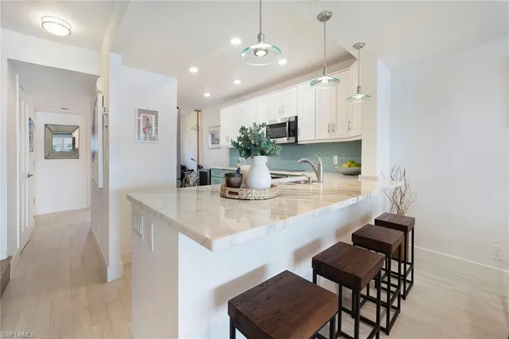 Kitchen with a peninsula, tasteful backsplash, white cabinets, light stone countertops, and a breakfast bar