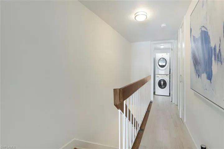 Hall with stacked washer and clothes dryer, light wood finished floors, and an upstairs landing
