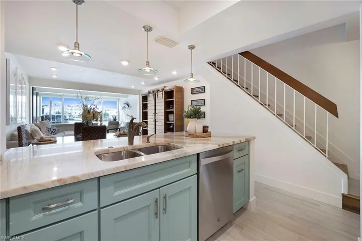 Kitchen featuring light stone countertops, stainless steel dishwasher, light wood-style floors, hanging light fixtures, and open floor plan