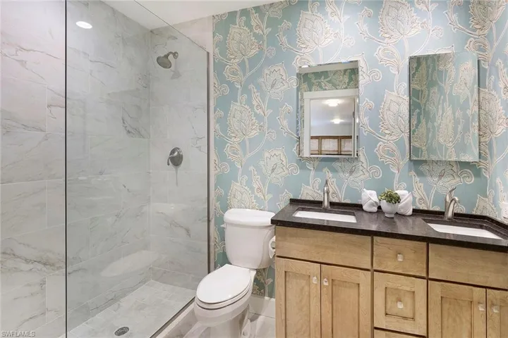 Full bath featuring wallpapered walls, double vanity, and tiled shower