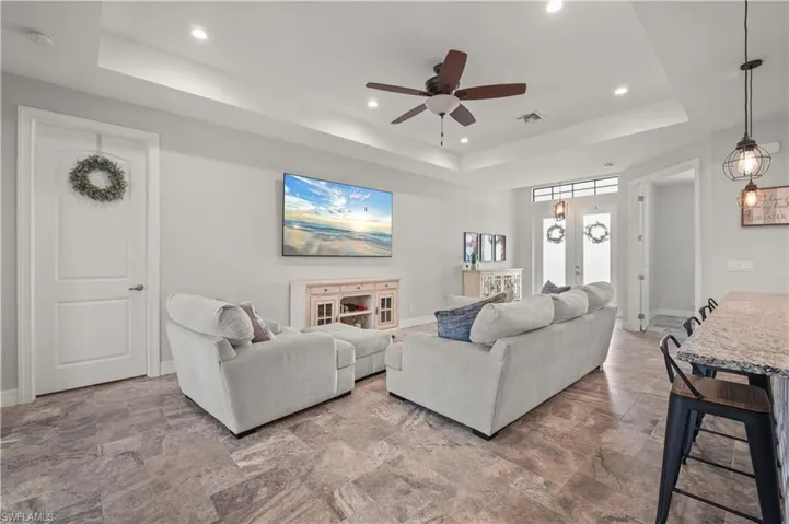 Living room featuring a ceiling fan, a raised ceiling, recessed lighting, and light stone finish flooring