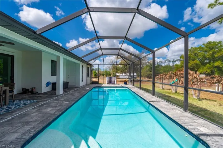 Outdoor pool featuring a patio area, a sunroom, glass enclosure, and a lawn