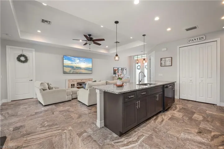 Kitchen with open floor plan, ceiling fan, a tray ceiling, light stone counters, and an island with sink