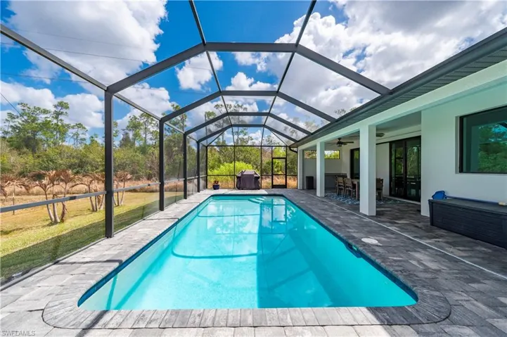 Swimming pool with glass enclosure, a patio area, a sunroom, and a lawn