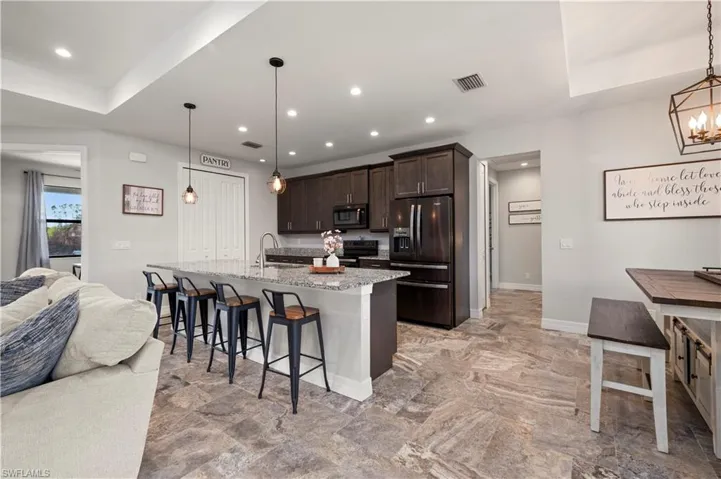 Kitchen with a kitchen breakfast bar, dark wood finish cabinetry, black appliances, open floor plan, and a center island with sink