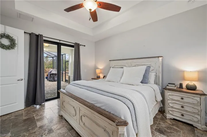 Bedroom featuring a raised ceiling, stone tile flooring, access to exterior, and a ceiling fan