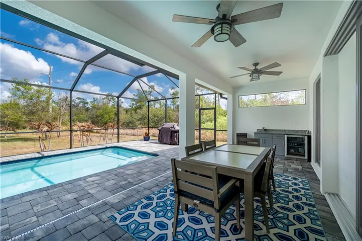 Swimming pool featuring glass enclosure, a patio area, an outdoor kitchen / dining area, and a sunroom