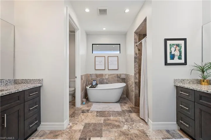 Bathroom with vanity, a shower stall, a freestanding tub, light stone finish floors, and recessed lighting