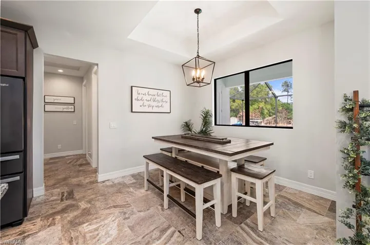 Dining space with hanging lights, a tray ceiling, and light stone finish flooring