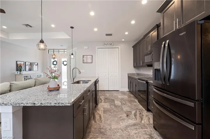 Kitchen with black appliances, open floor plan, light stone counters, and dark wood finish cabinetry