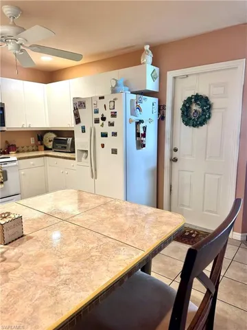 Kitchen with white cabinets, white appliances, light tile patterned floors, ceiling fan, and a breakfast bar area