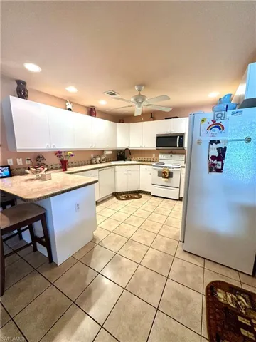 Kitchen featuring white appliances, white cabinetry, light tile patterned floors, a kitchen bar, and recessed lighting