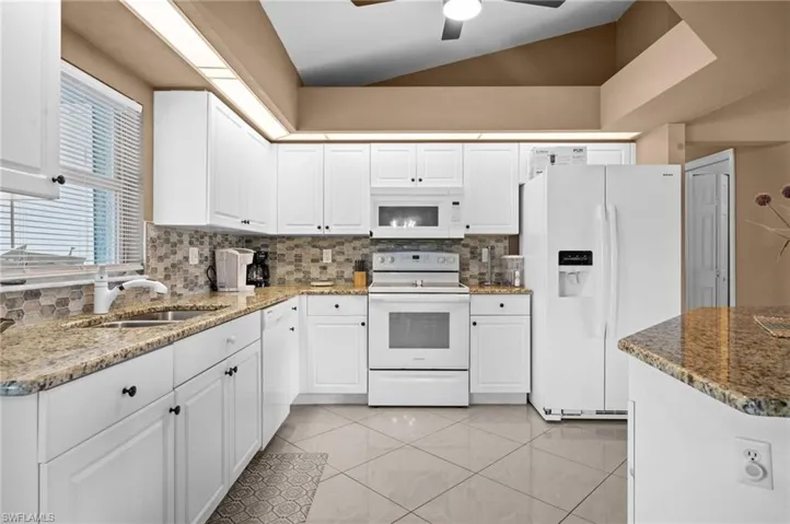 Kitchen featuring white appliances, white cabinets, dark stone countertops, a ceiling fan, and light tile patterned flooring