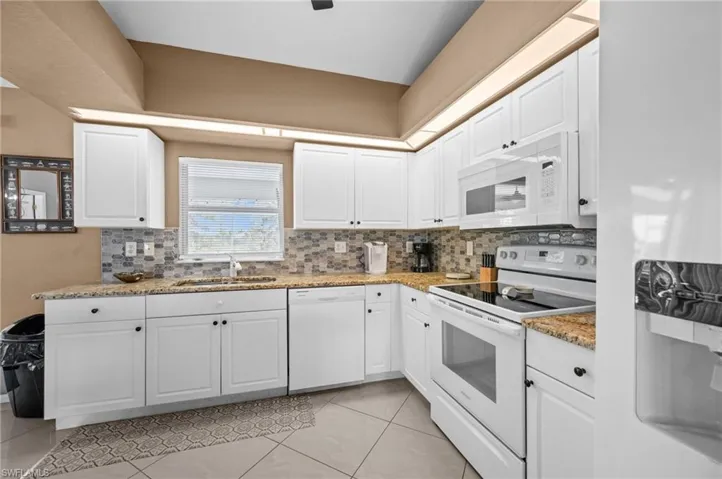 Kitchen featuring white appliances, white cabinetry, light stone countertops, and tasteful backsplash
