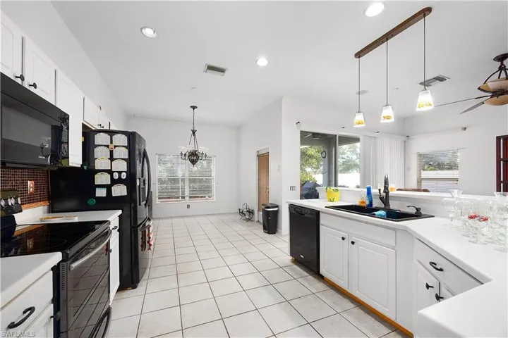 Kitchen featuring white cabinets, black appliances, light countertops, hanging light fixtures, and plenty of natural light