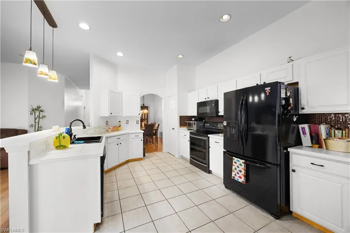 Kitchen with arched walkways, light countertops, black appliances, a peninsula, and white cabinetry