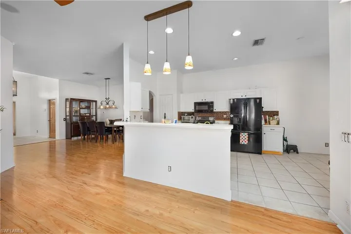 Kitchen with black appliances, tasteful backsplash, hanging light fixtures, white cabinetry, and arched walkways