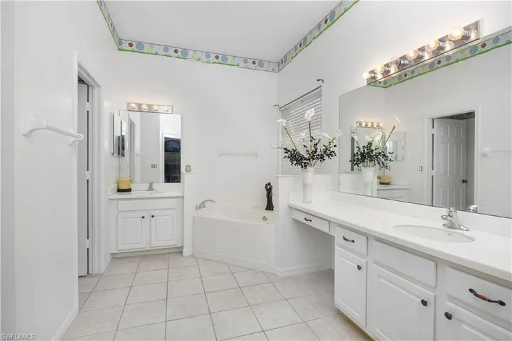 Bathroom with two vanities, light tile patterned floors, and a garden tub