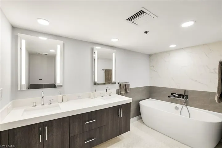 Bathroom with tile walls, double vanity, a freestanding bath, and recessed lighting