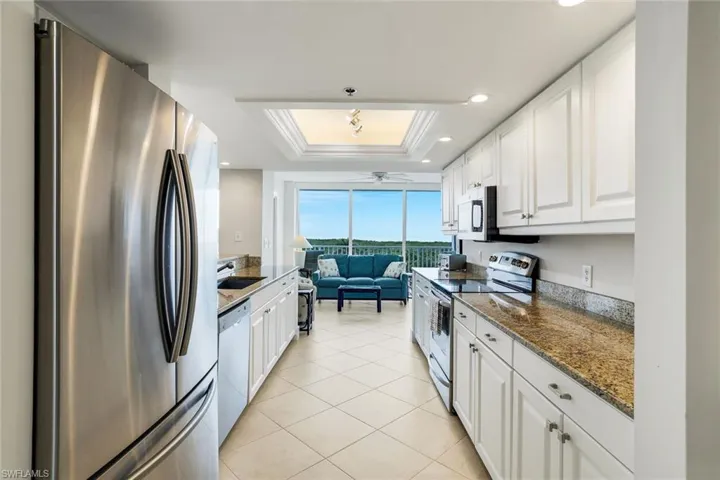 Kitchen featuring stainless steel appliances, white cabinets, a tray ceiling, dark stone countertops, and crown molding
