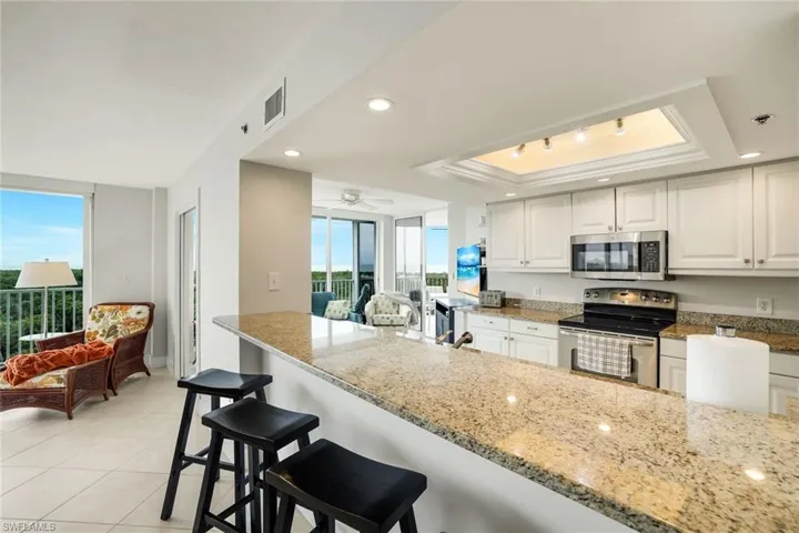 Kitchen with white cabinetry, stainless steel appliances, light stone countertops, a kitchen bar, and a raised ceiling