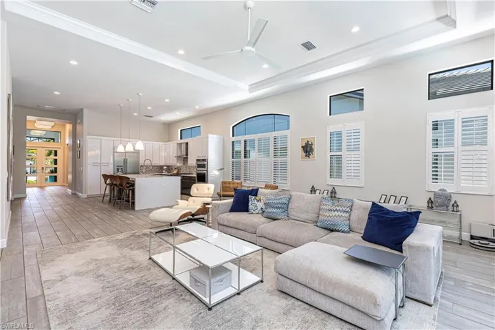 Living area featuring light wood finished floors, ornamental molding, recessed lighting, a ceiling fan, and a tray ceiling