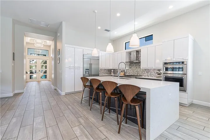 Kitchen with stainless steel appliances, light wood finished floors, a kitchen island with sink, white cabinets, and tasteful backsplash