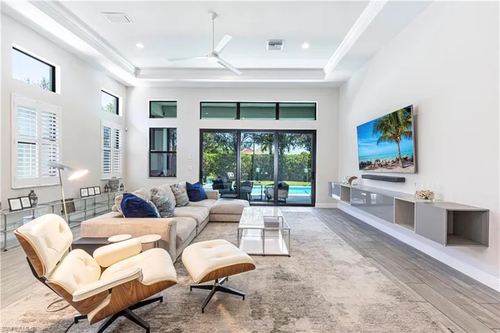 Living area featuring a towering ceiling, ceiling fan, wood finished floors, ornamental molding, and baseboards