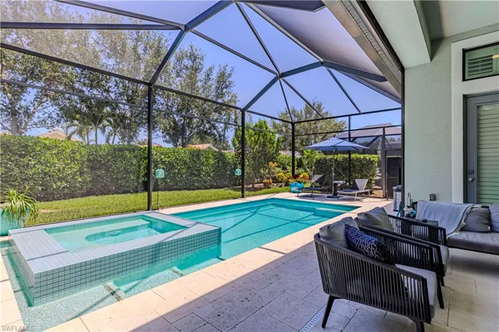 Outdoor living space with screen enclosure, and a pool with connected hot tub and lush landscaping