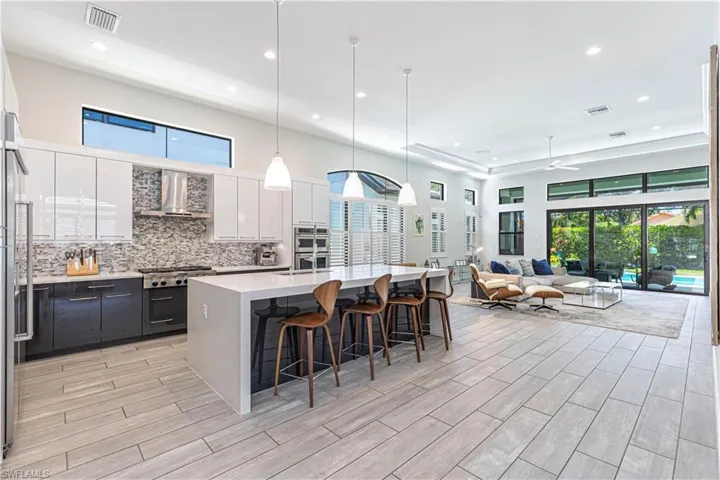 Kitchen featuring wall chimney range hood, stainless steel appliances, recessed lighting, white cabinets, and a breakfast bar area