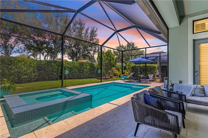 Pool at dusk with outdoor lounge area, a patio area, a pool with connected hot tub, and glass enclosure