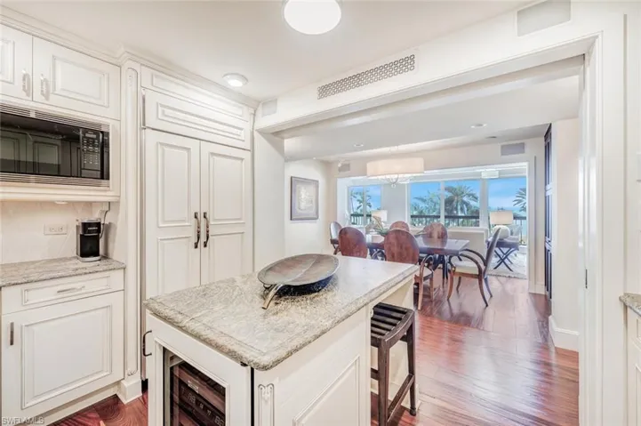 Kitchen with hardwood / wood-style floors, white cabinets, light stone counters, decorative backsplash, and black microwave